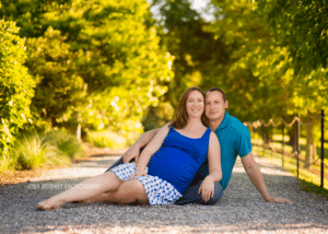 A couple expecting their first baby sitting down on a gravel path.