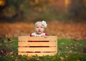 Photo of a baby girl sitting in a wooden box.