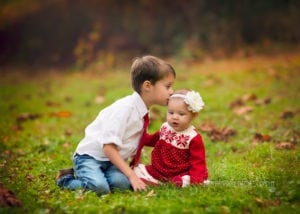 Professional photo of a brother and sister in Christmas outfits. Brother is kissing the baby girl.