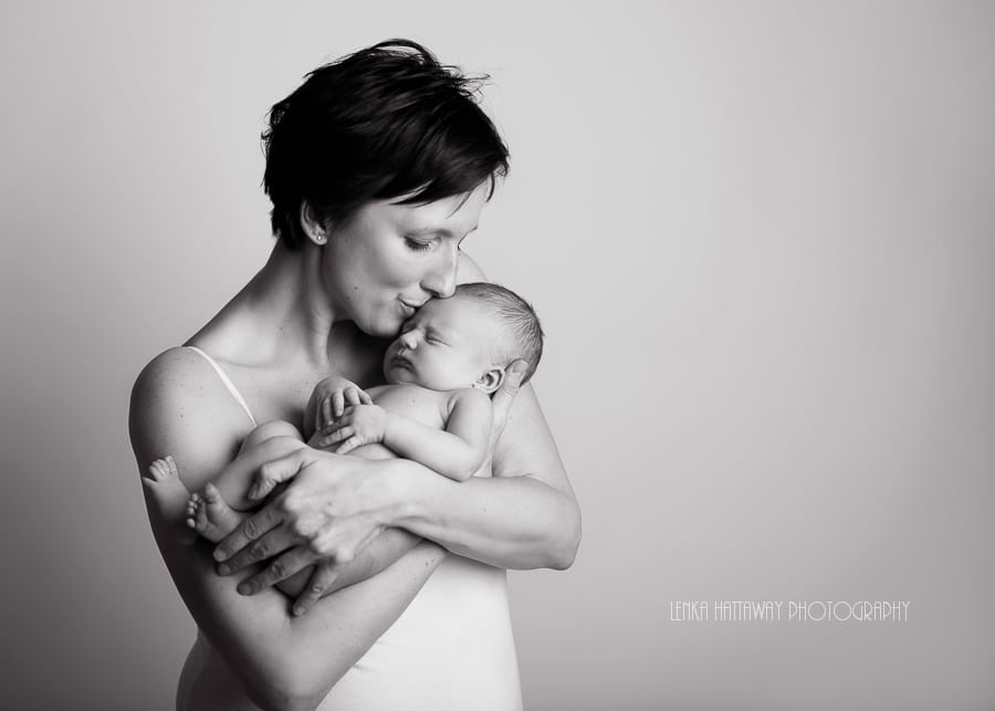 A black and white image of a new mom holding and kissing her newborn baby.