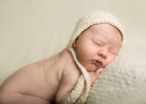 A close-up of a newborn baby girl in a white cap.