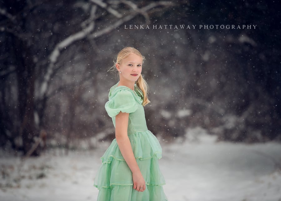 Beautiful winter image of a girl in a green dress while snow is falling.