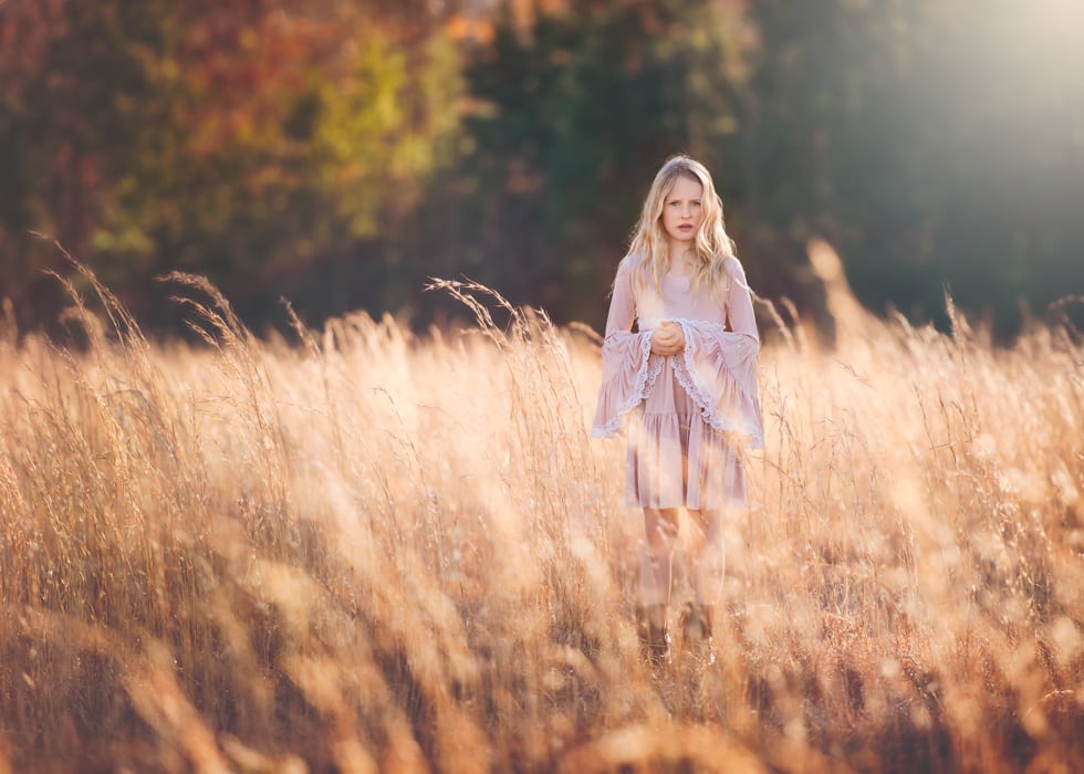 A dreamy photo of a girl standing in tall grass with beautiful light all around.