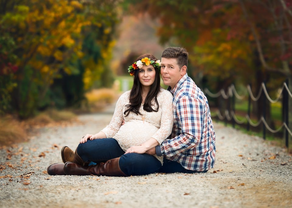 A couple sitting on the ground at the Asheville Arboretum. Fall colors, woman is expecting a baby.