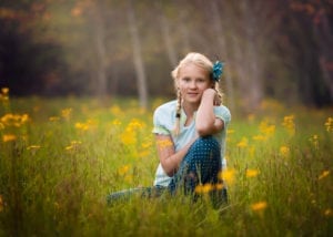 A girl sitting in a grass with flowers all around her.