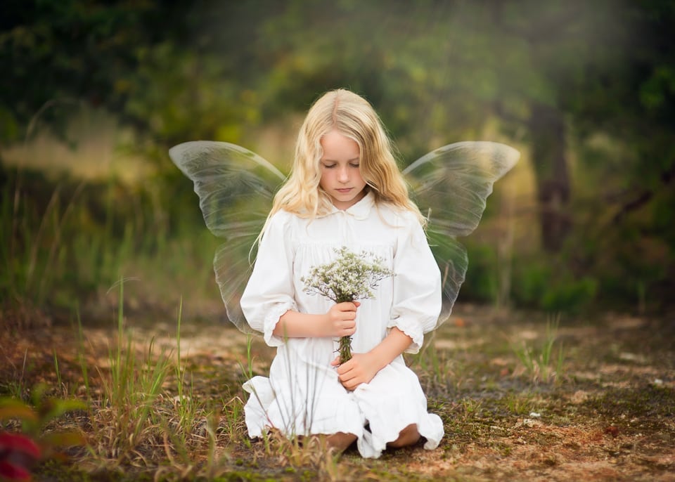 A photo of a girl with fairy wings holding flowers.