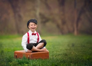 A professional image of a boy sitting on a suitcase.