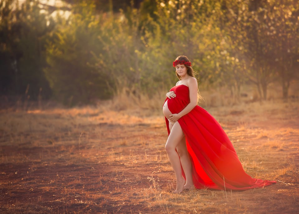 A beautiful maternity photo of an expecting mom in a red flowy gown.