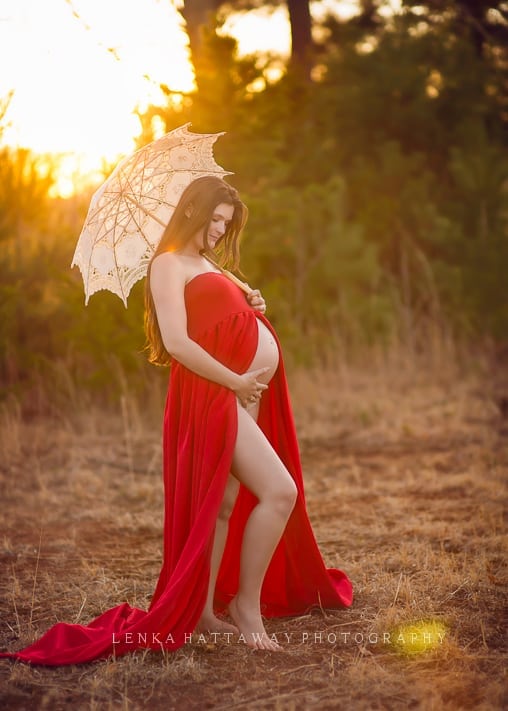 Pregnant mama looking down and holding her belly. In her other hand she is holding a beautiful parasol.