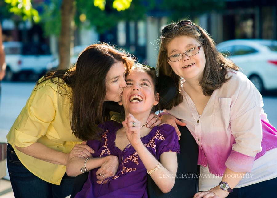 A sweet close-up photo of a mom with her two dughters. One of the daughters is on a wheelchair.