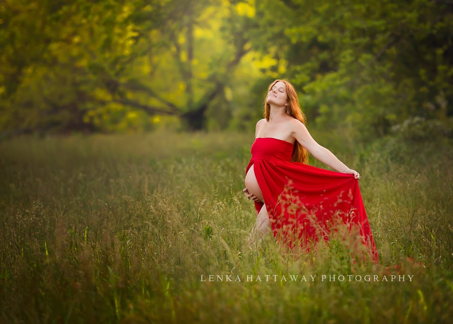 A beautiful dreamy maternity shot of an expecting mother dressed in a flowy red dress partially showing her belly.