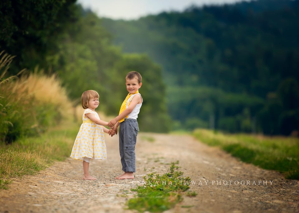 Two cute little children standing on a dirt road holding hands.