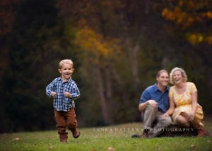 A professional photo of a boy running and his parents in the background watching him.