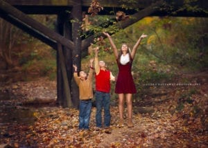 Three siblings playing with leaves, throwing them up in the air.