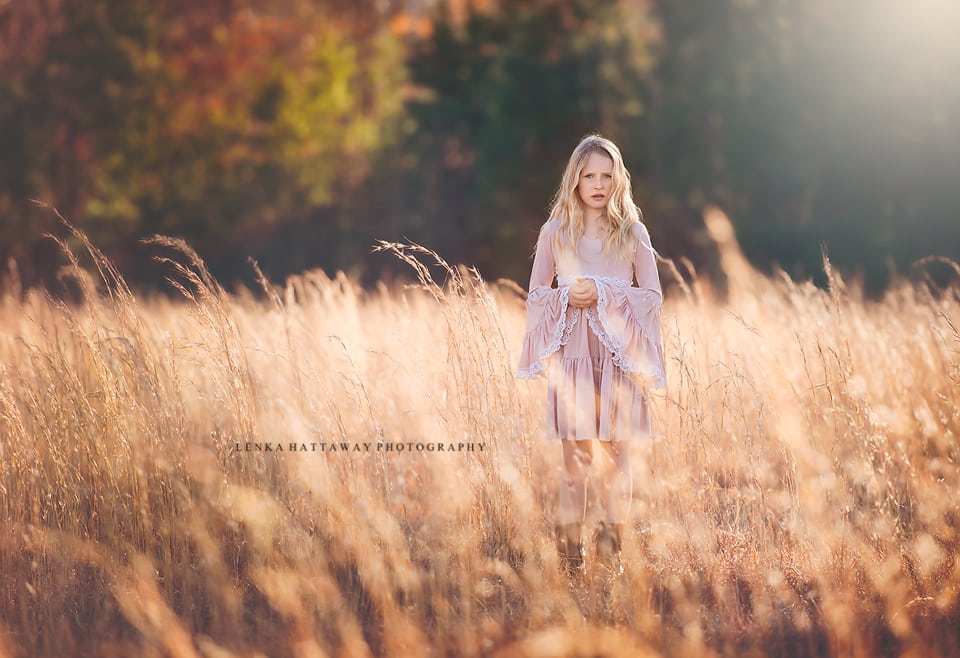 A professional image of a child in a pink dress standing in a tall grass, beautifully lit.