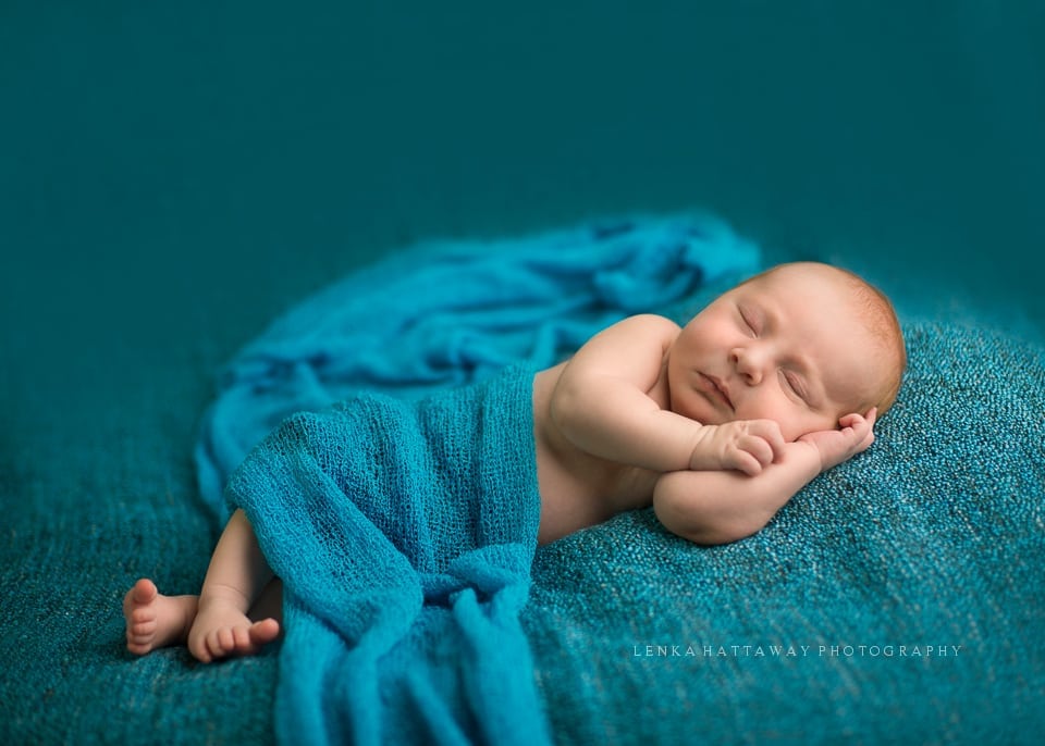 A professional photo of a newborn baby sleeping on a blue blanket.