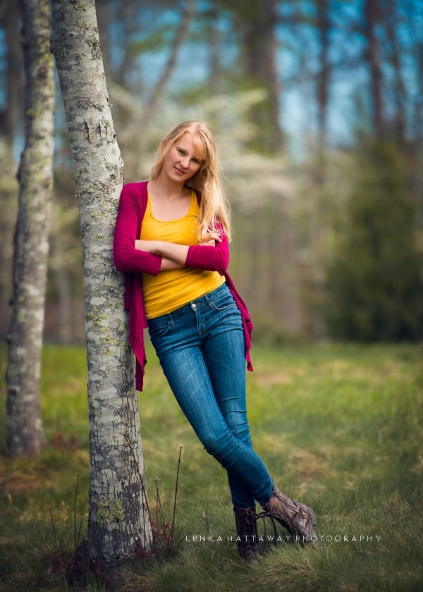 A teen girl standing porped against a tree.