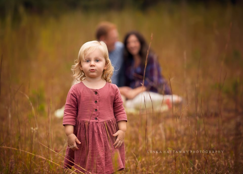 A photo of a little girl with parents sitting in the background.