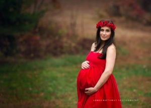 A close-up maternity photo of a woman dressed in red gown and wearing a flower crown.