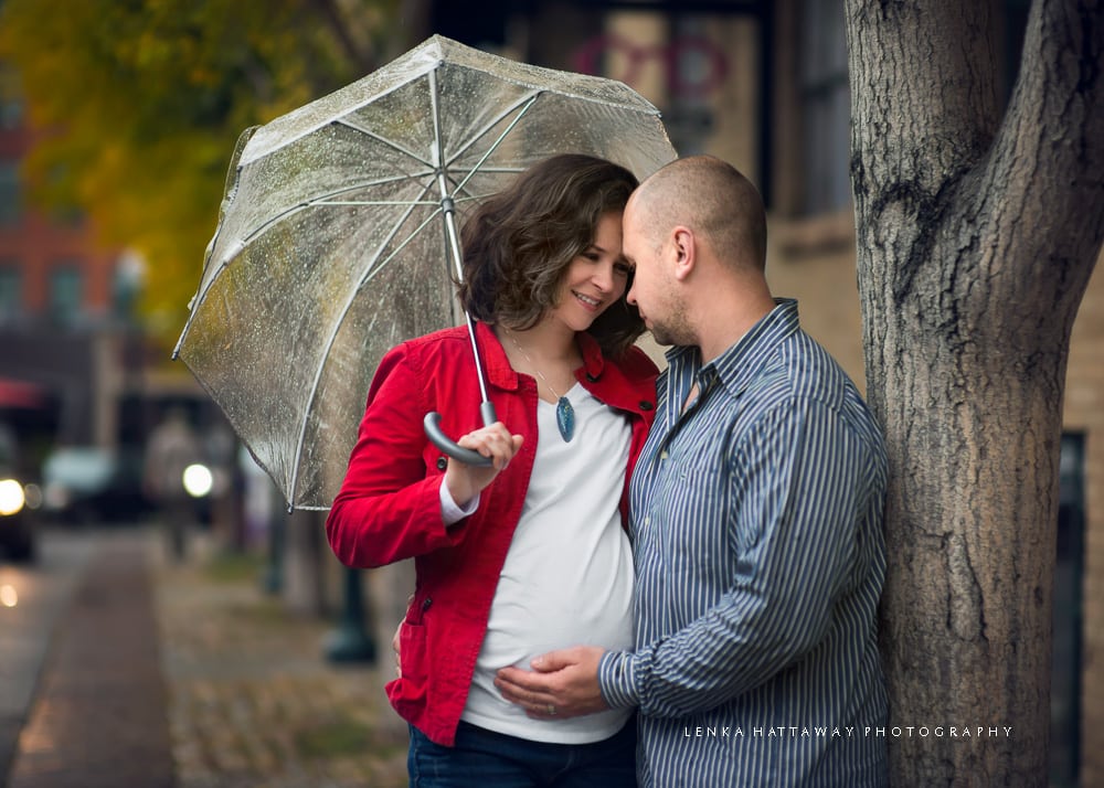 Pregnant couple standing close together holding and umbrella.