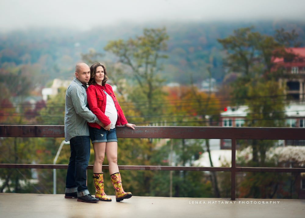 Photo of an expecting couple standing by railing downtown.