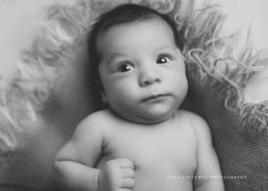 A black and white shot of a newborn baby with eyes open.