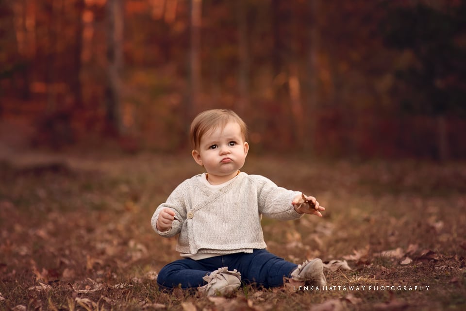 A photo of a sweet baby girl sitiing down surrounded with fall leaves.