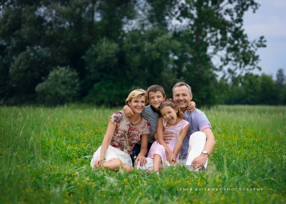 A family hugging and sitting together on grass surrounded by beautiful greenery.