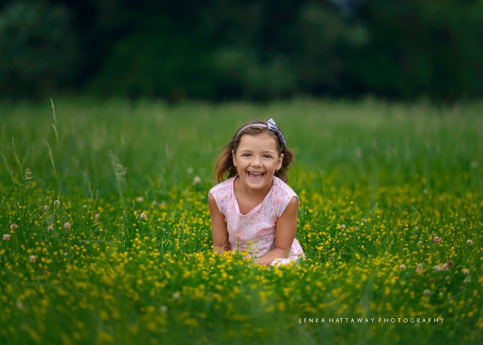 A girl sitting in green grass with yellow flowers.