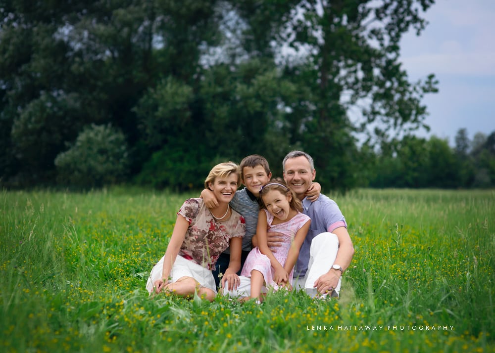 A photo of a family hugging and sitting together on grass surrounded by beautiful greenery.