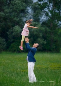 Playful family photo of a father throwing his child, his girl, up in the air.