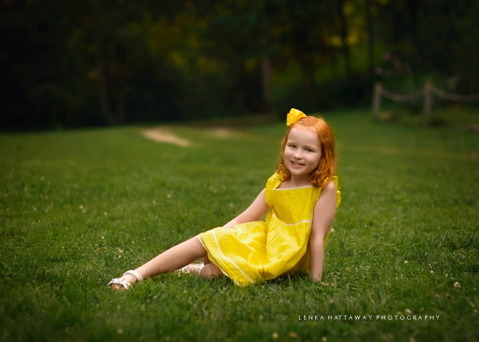 A red head girl in a yellow dress sitting on grass at the Botanical Gardens.