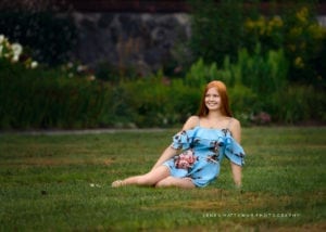Woman sits on grass during her senior photo session at the Biltmore Estate.
