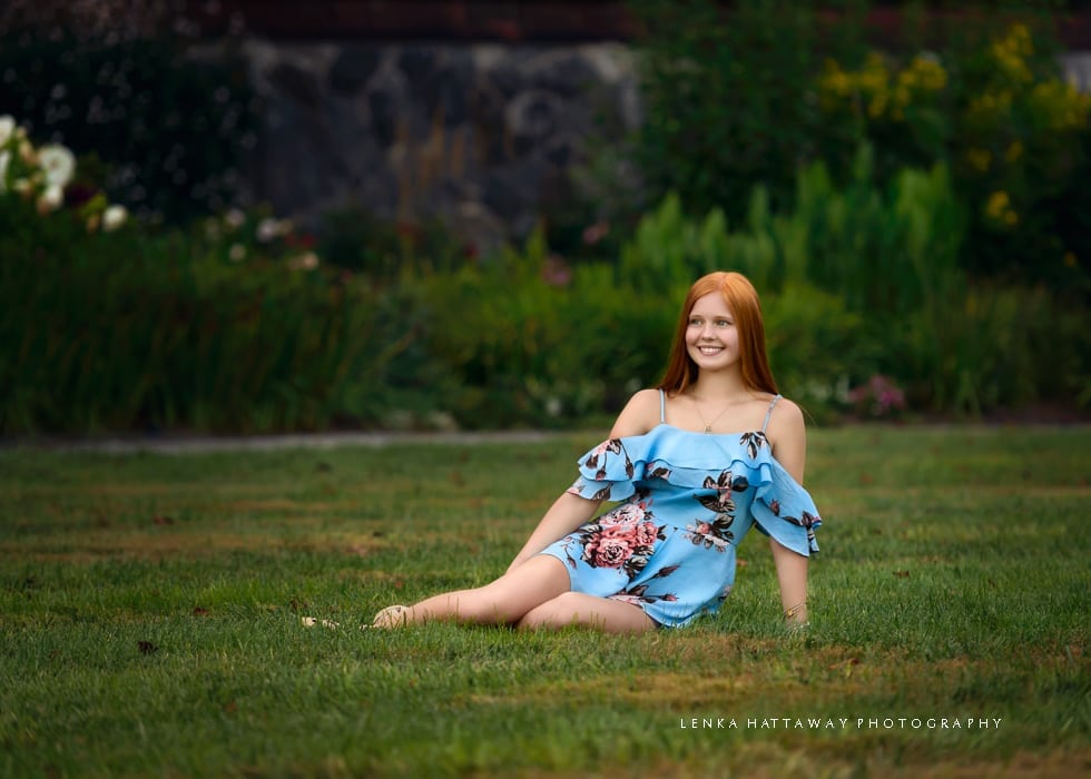 Woman sits on grass during her senior photo session at the Biltmore Estate.