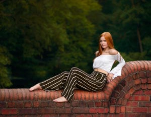 A high school senior portrait of a lovely girl being propped up on a brick bridge railing.