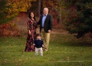 A baby walking in front of his parents during their fall mini session at the Arboretum.