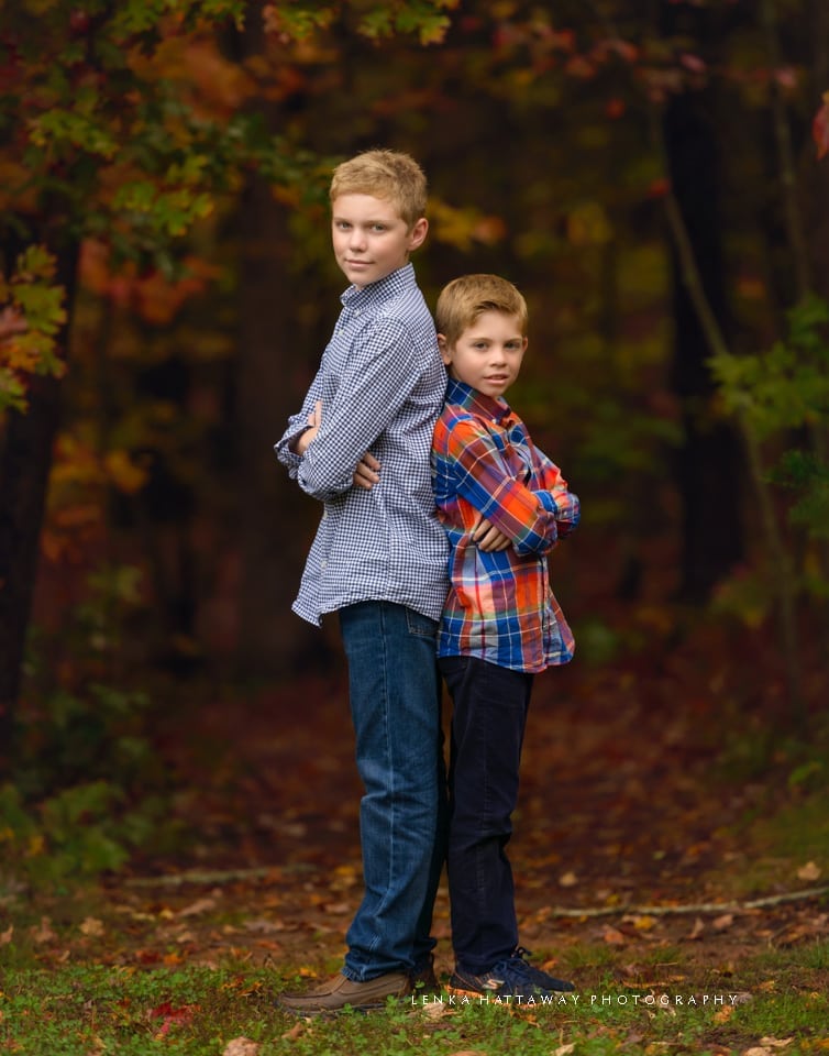 Brothers standing back to back surrounded by fall colors at the Asheville Arboretum.