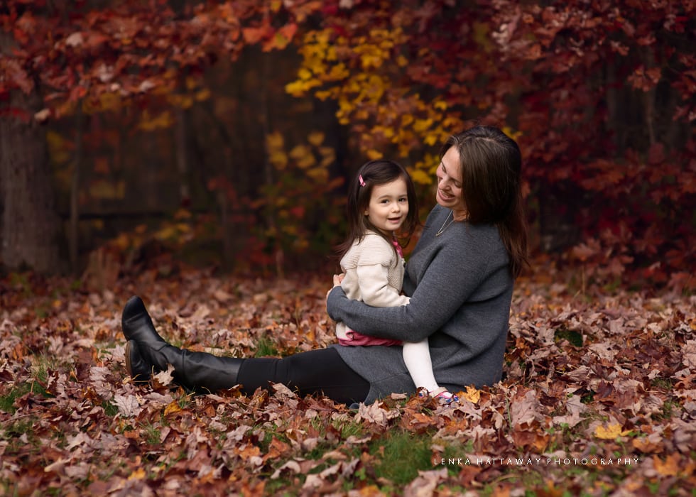 Mom and daughter sitting on the ground together surrounded by fall leaves in Asheville, NC.