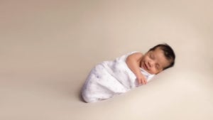 Sweet newborn photo of a baby boy wrapped in a blanket, smiling.