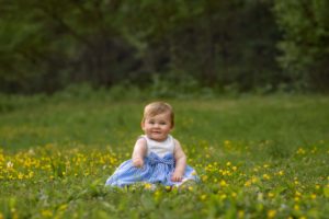 Adorable little baby girl sitting in grass with yellow flowers.