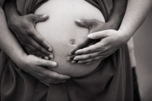 Black and white pregnant belly close-up with hands..