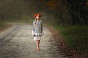 A dreamy photo of a girl wearing fall headpiece and walking on a road.
