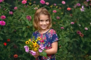 Child portrait of a girl holding pretty Black-eyed Susan flowers and Zenia flowers behind her.