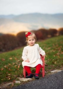 Baby girl sitting in a red chair with teh Blue Ridge Mountains in the background.