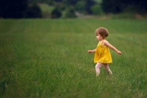 Sweet baby girl in a yellow dress walking in grass.