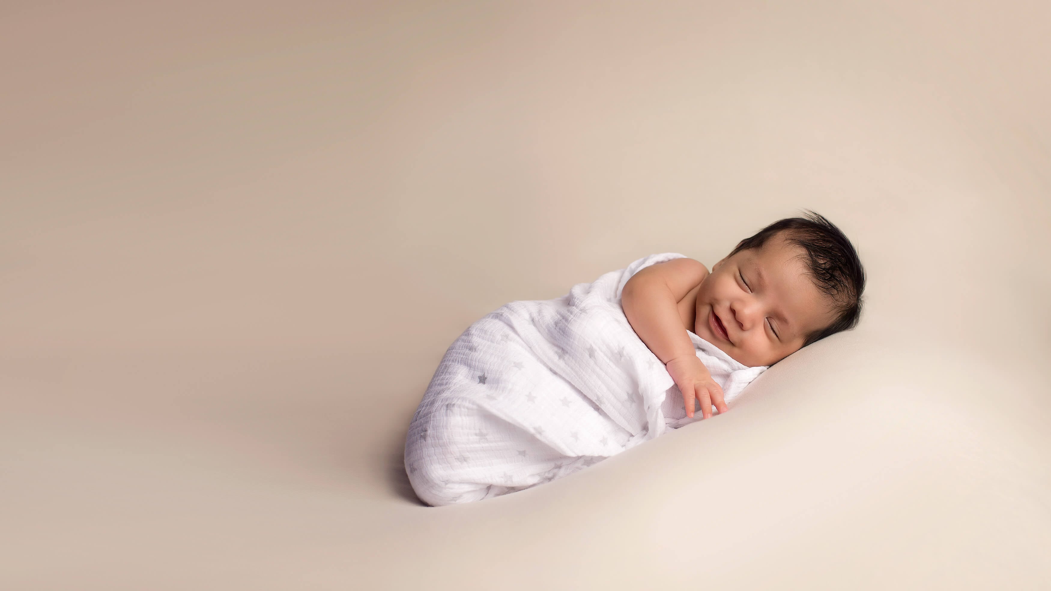 Newborn baby boy wrapped in a blanket, smiling.