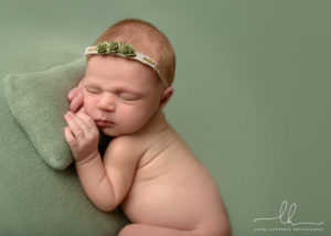 Newborn baby photo lying on green blanket and pillow.