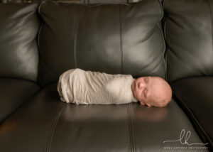 Newborn baby, wrapped and laying on a couch.