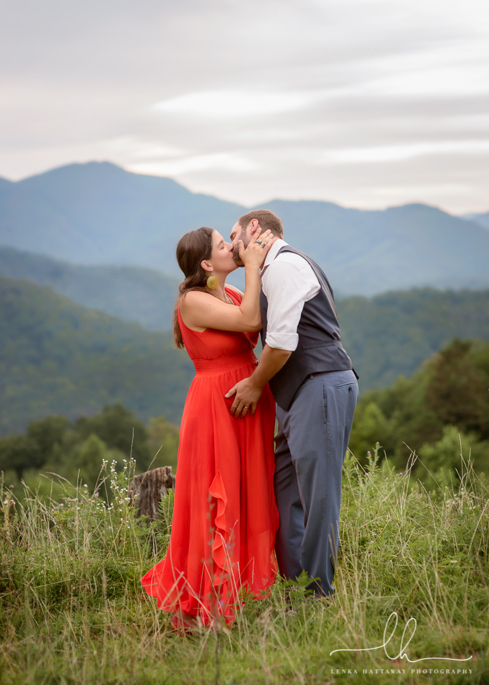 Expecting couple kissing with mountains in the background.