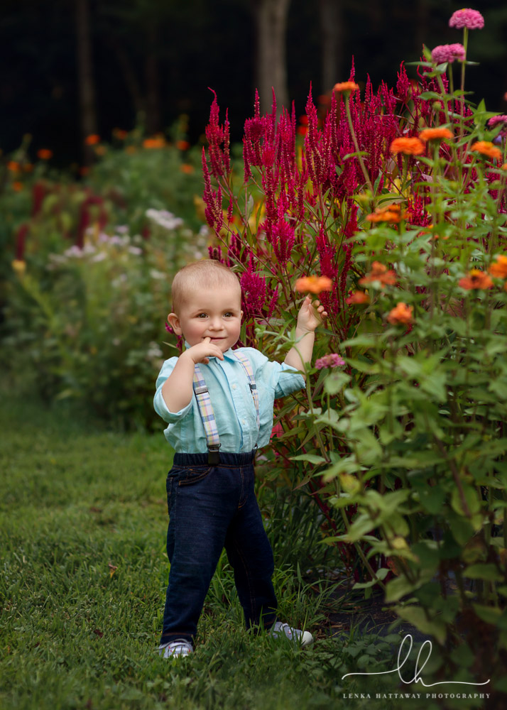 Little boy standing next to colorful flowers.